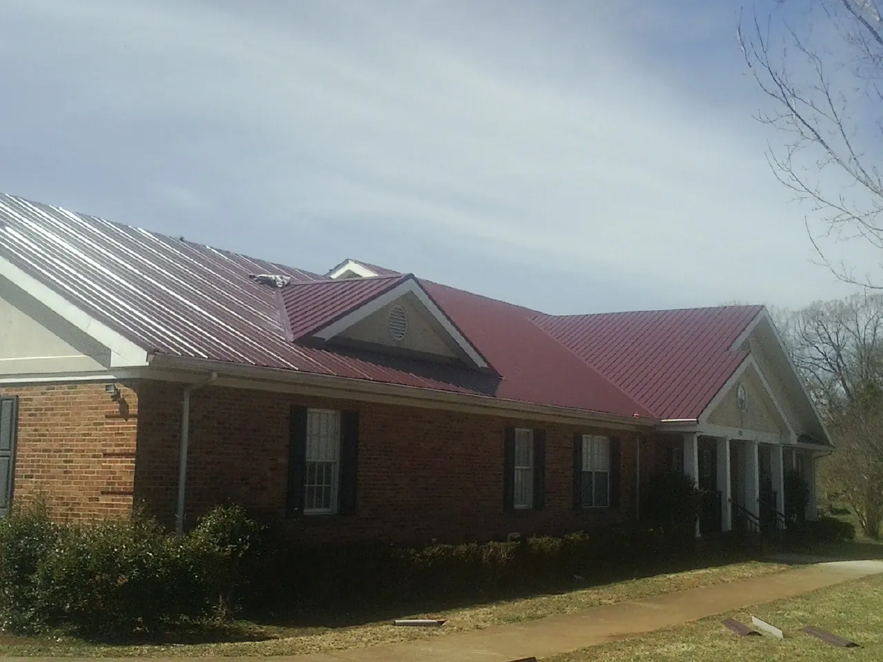 Red metal roof with gabled entries on a long brick building, from a Hail Damage Roof Repair job in New Haven